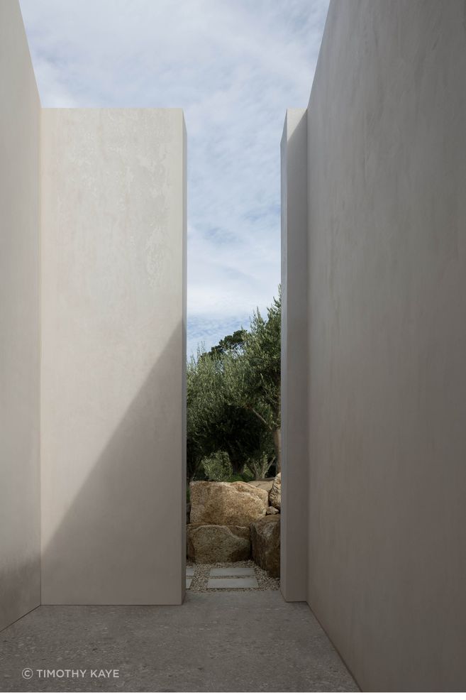 A narrow passage between monolithic walls choreographs a moment of compression, drawing attention to light, shadow and the landscape beyond.