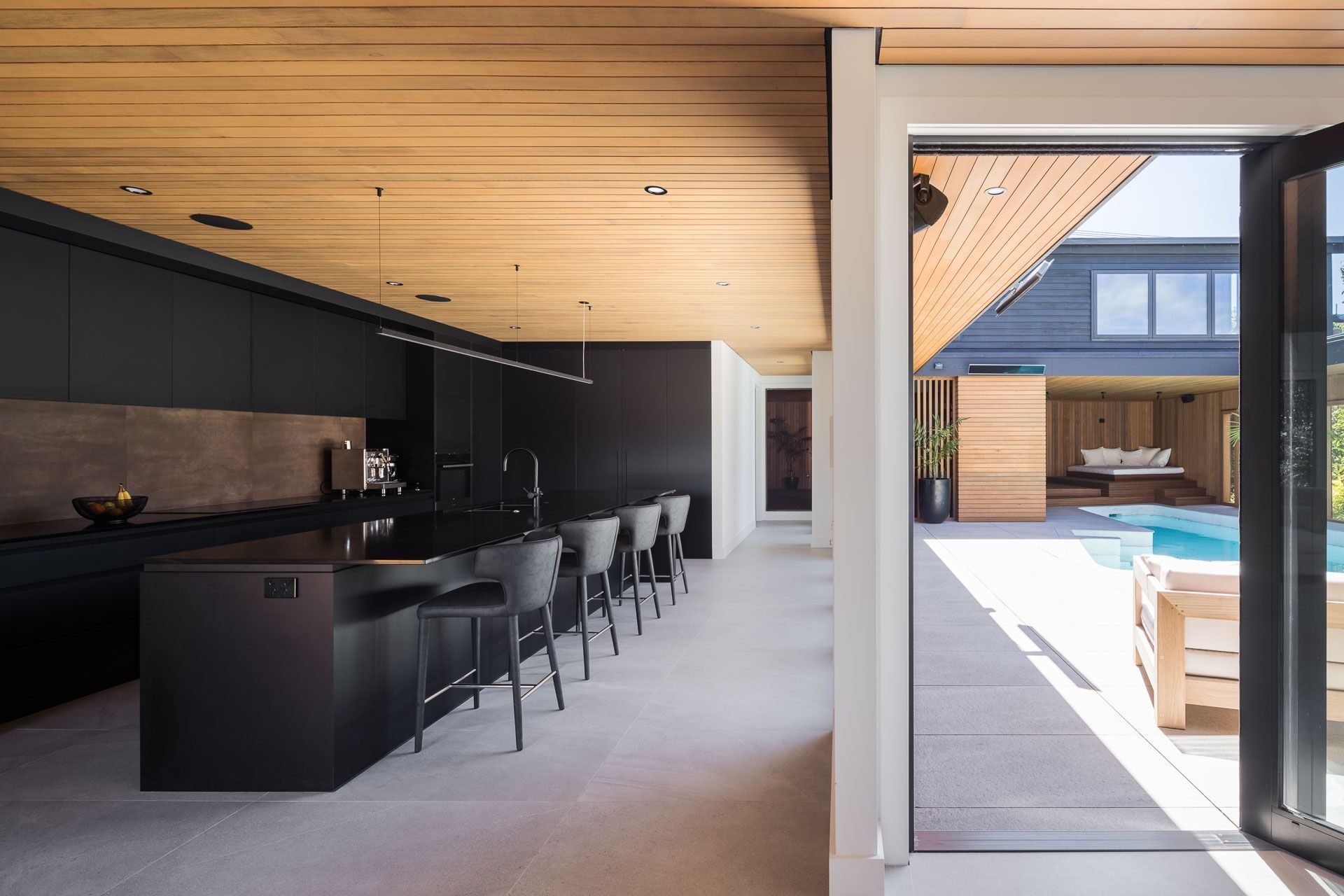The jet-black kitchen is striking in contrast to the warm-toned cedar and subdued grey tiles.