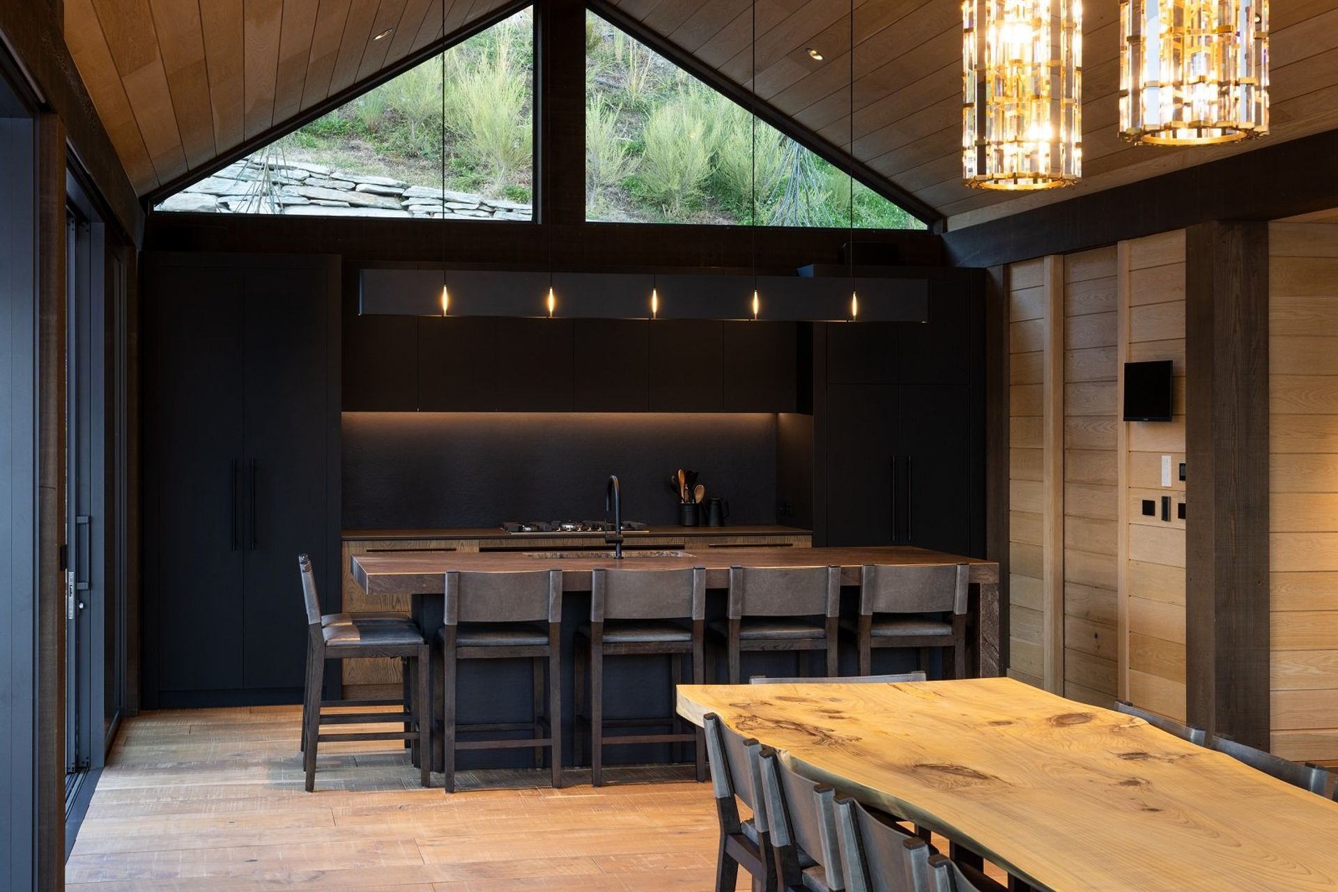 Adjacent to the main living space, the kitchen, with its dark and moody colour palette, is recessed back towards the hill.