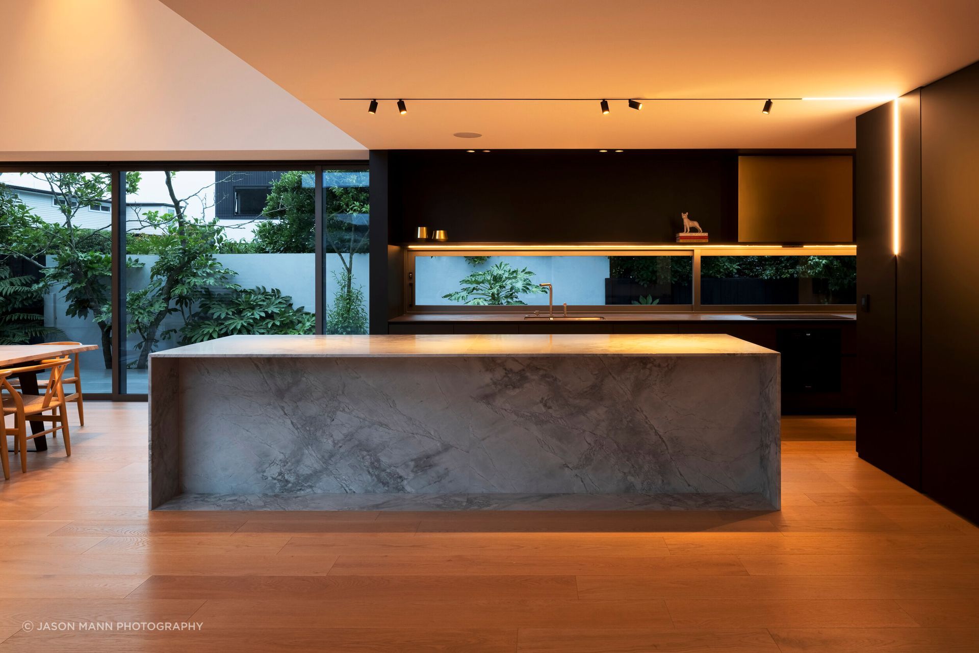 The kitchen is centrally positioned in the flattened 'T' shape arrangement, spilling into two living areas with distinct spatial experiences. 