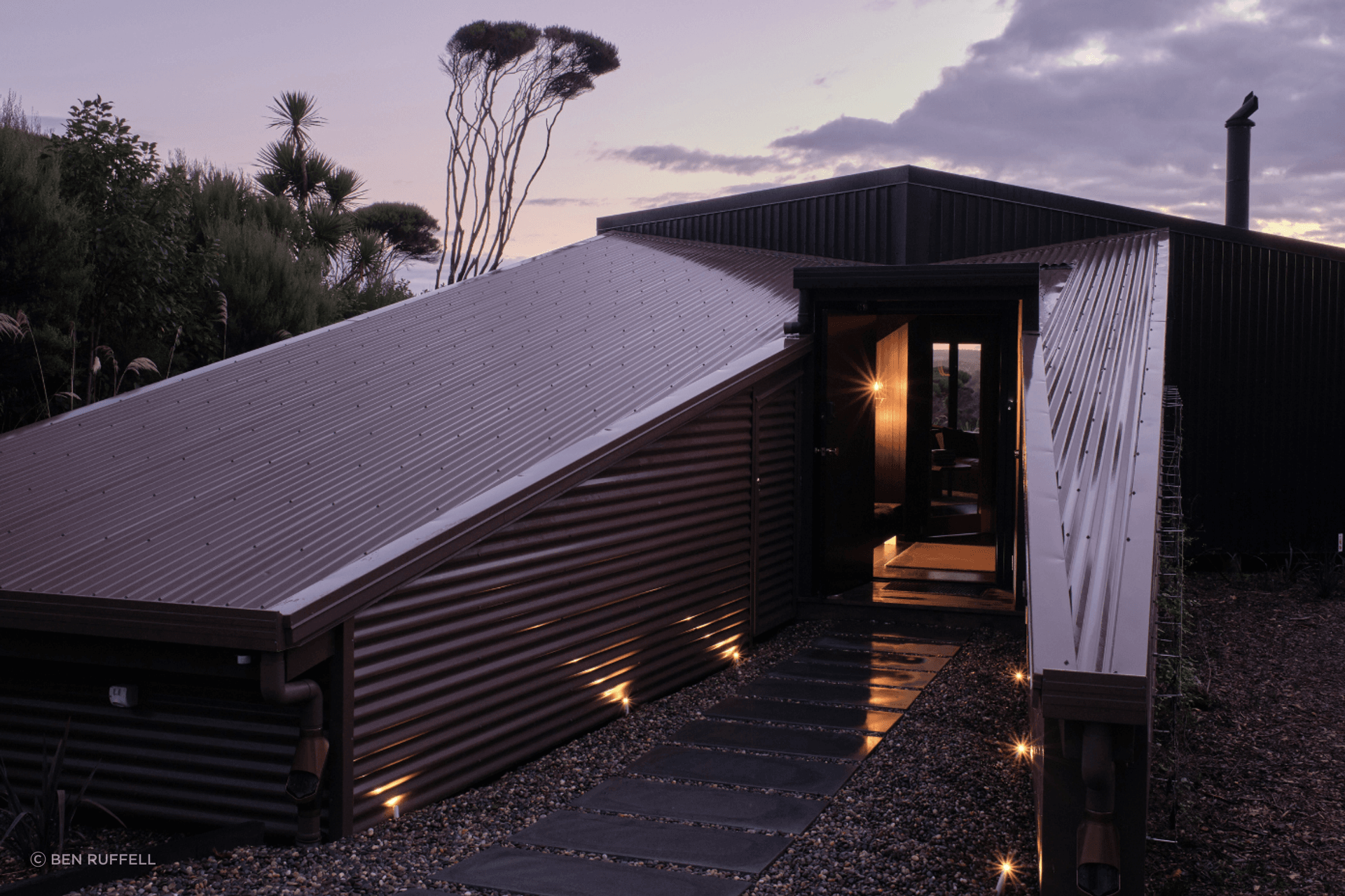 Upon arrival, the home is low to the land, consisting of one brown structure and one black, which lean to meet one another. The brown structure is split to create a protective passageway to the entry.