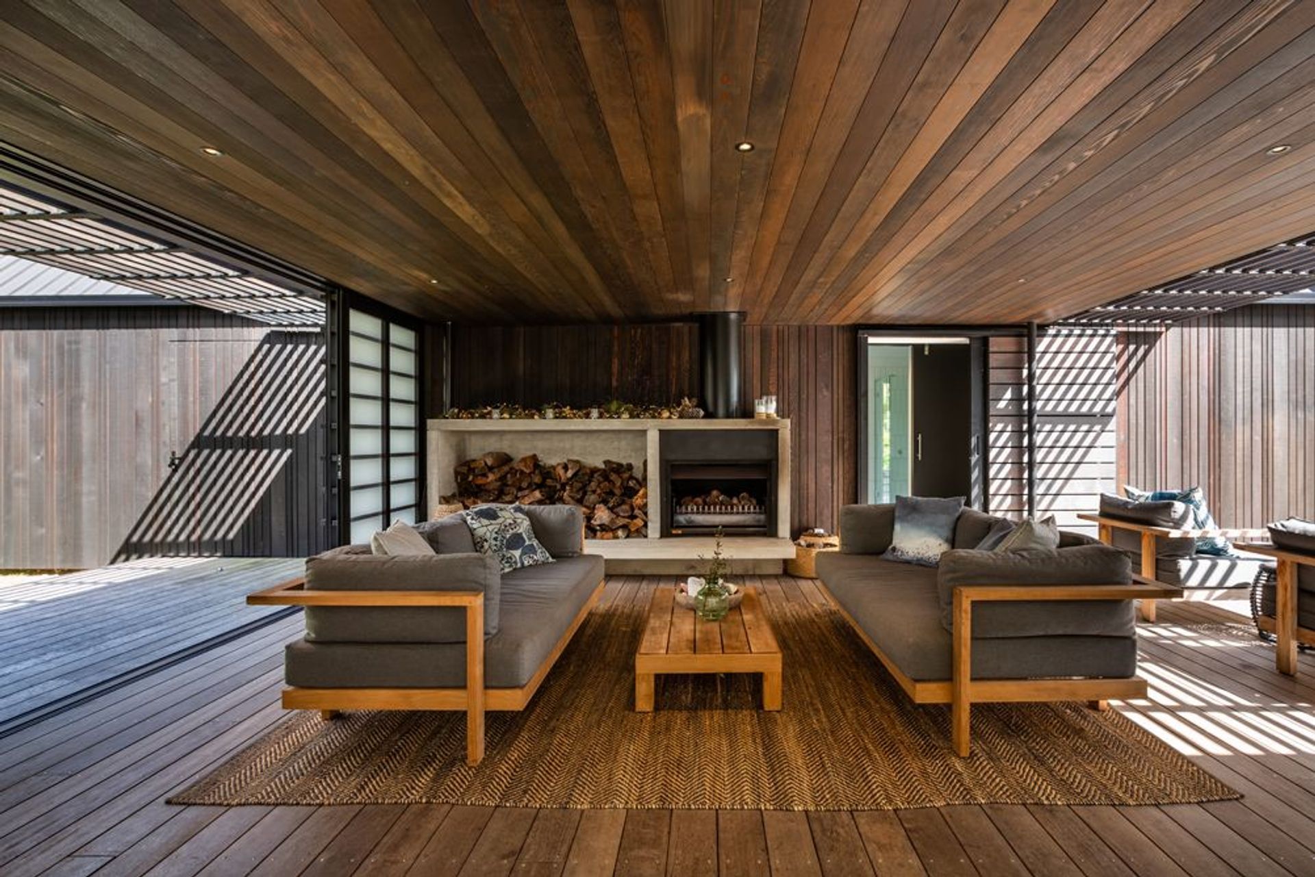 Here, a sheltered space dances the line between indoors and out and houses a large outdoor fire whose chimney punctuates the cedar-lined roof