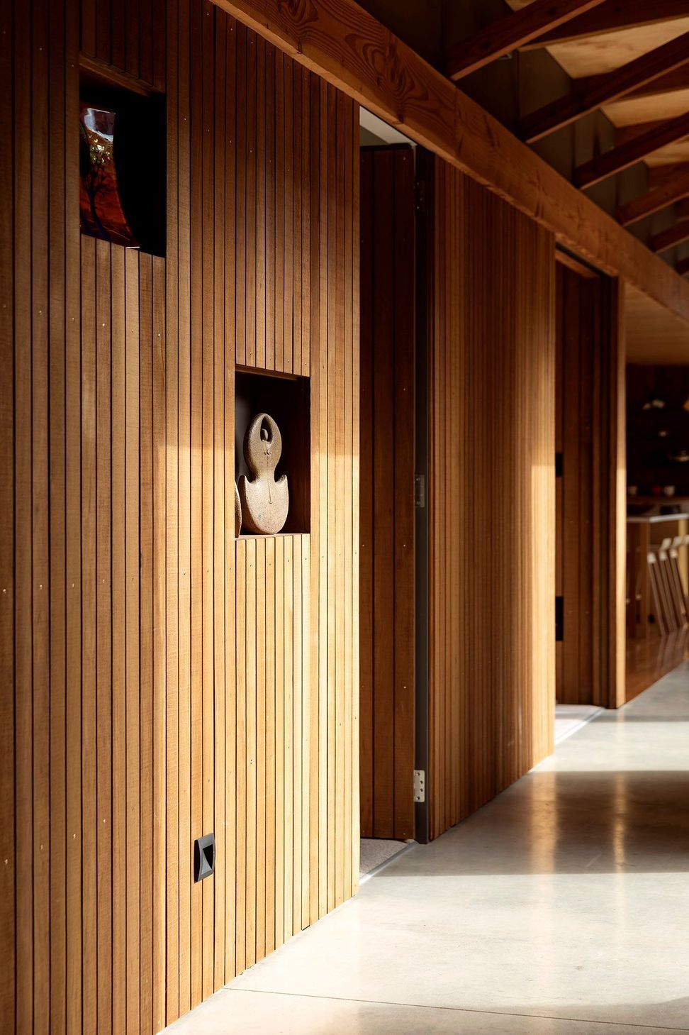 Beginning in the kitchen and winding through the entire central corridor, including the doors that lead into the bedrooms off it, the walls are clad in vertical shiplap totara that reaches up to meet the exposed timber ceiling.