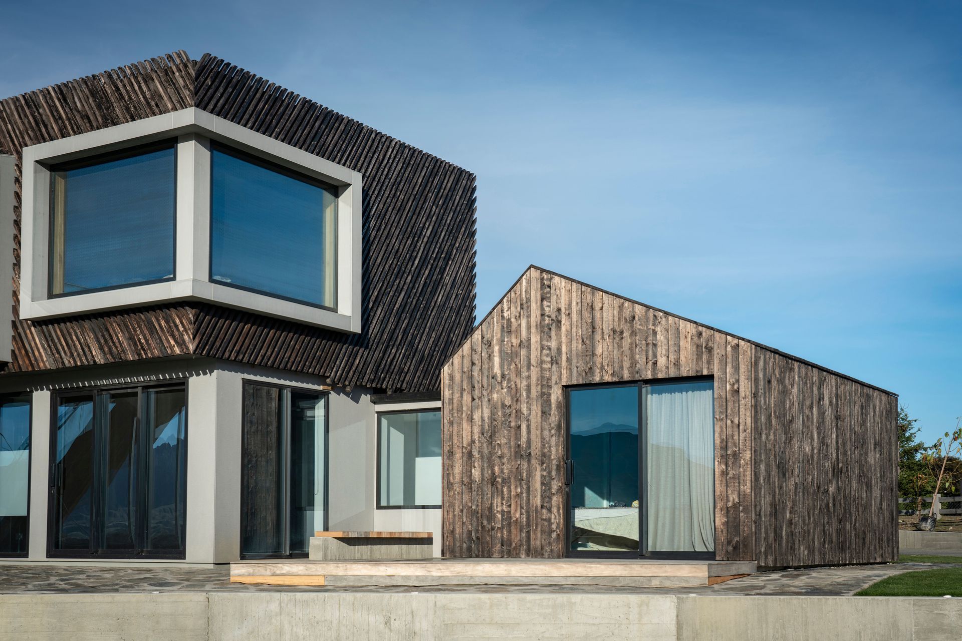  A recessed corner window creates a dramatic aperture in the upper storey façade. Sliding doors in the bedroom wing open out to a deck and overlook the tennis court.