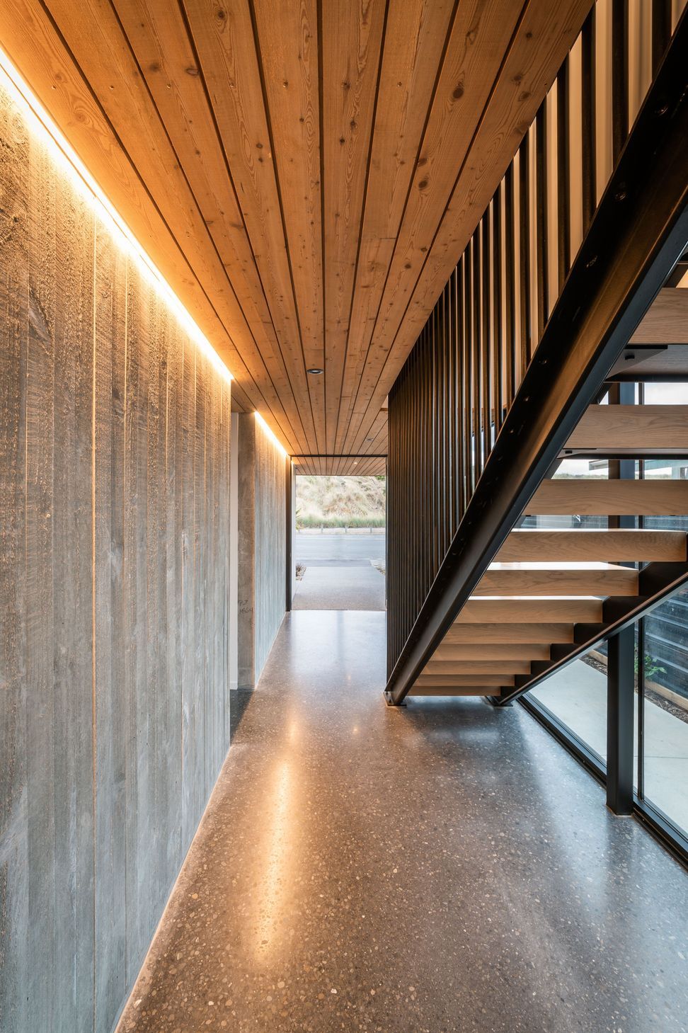 A board form concrete wall, larch ceiling and and black steel balustrades define the lower hallway 