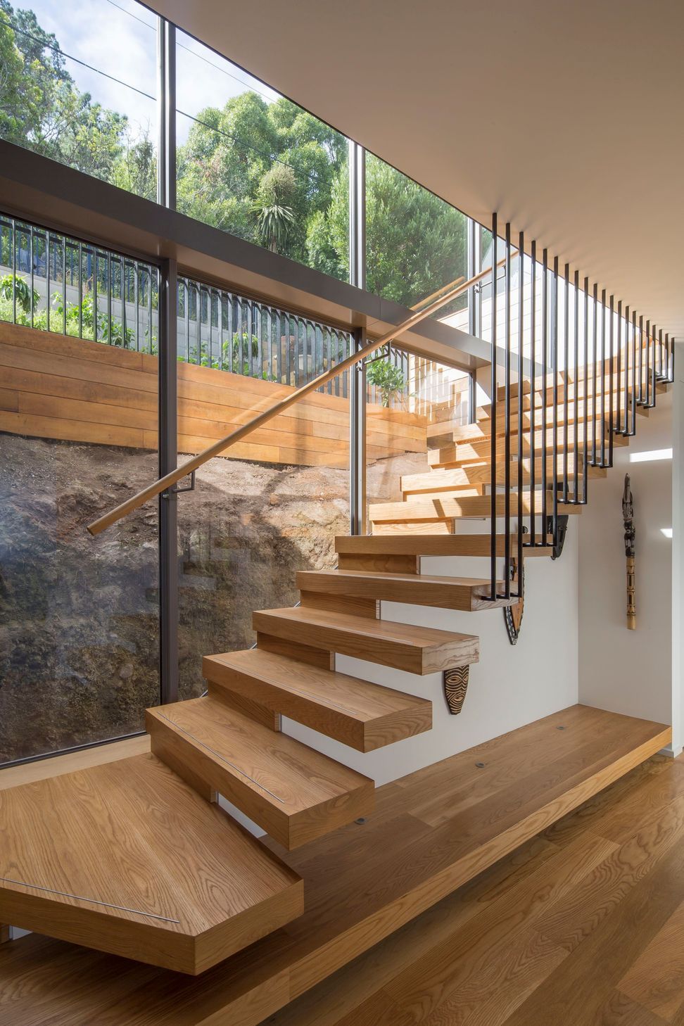Double-height glazing behind the main, cantilevered, staircase shows how the house is sitting shy of the rockface behind.