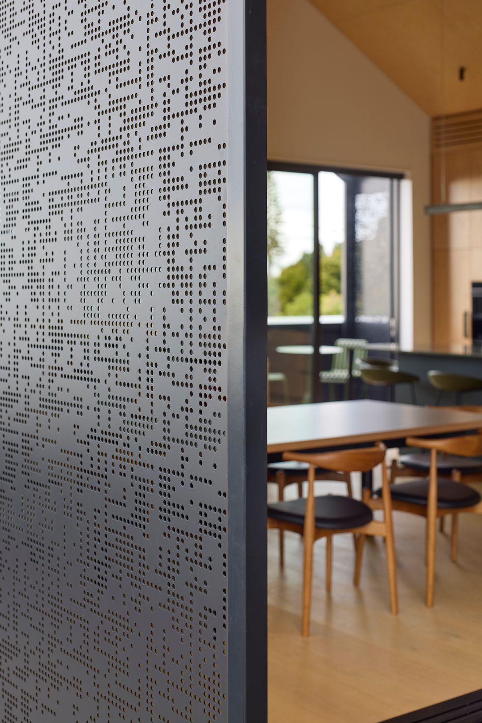 A close-up of the operable metal screens demonstrates how the home can open or close in response to climate and privacy. Beyond, the open-plan kitchen, dining and living spaces are visible.