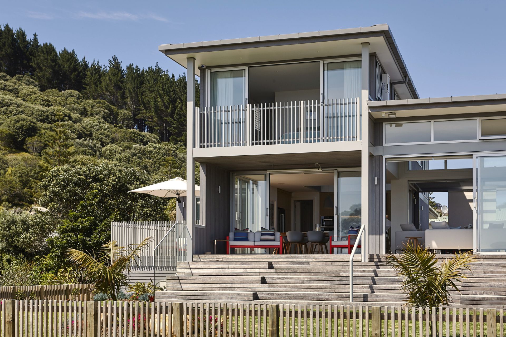 Viewed from the approach, the home's glazed front elevation welcomes natural light deep into the interior. Native planting softens the contemporary architecture, allowing the house to settle naturally within its coastal setting.