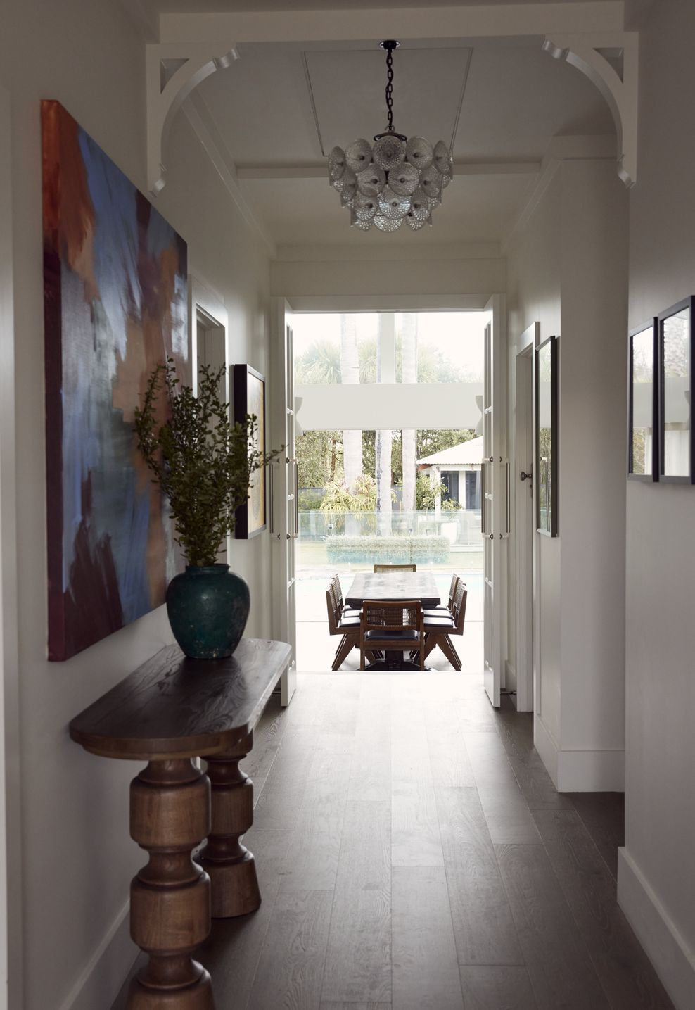 The entry hall at Point Chevalier Bungalow — Kinkeldey mid-century chandelier, large format artwork and a view straight through to the dining area and pool beyond. In collaboration with Hannah Warren Interiors.