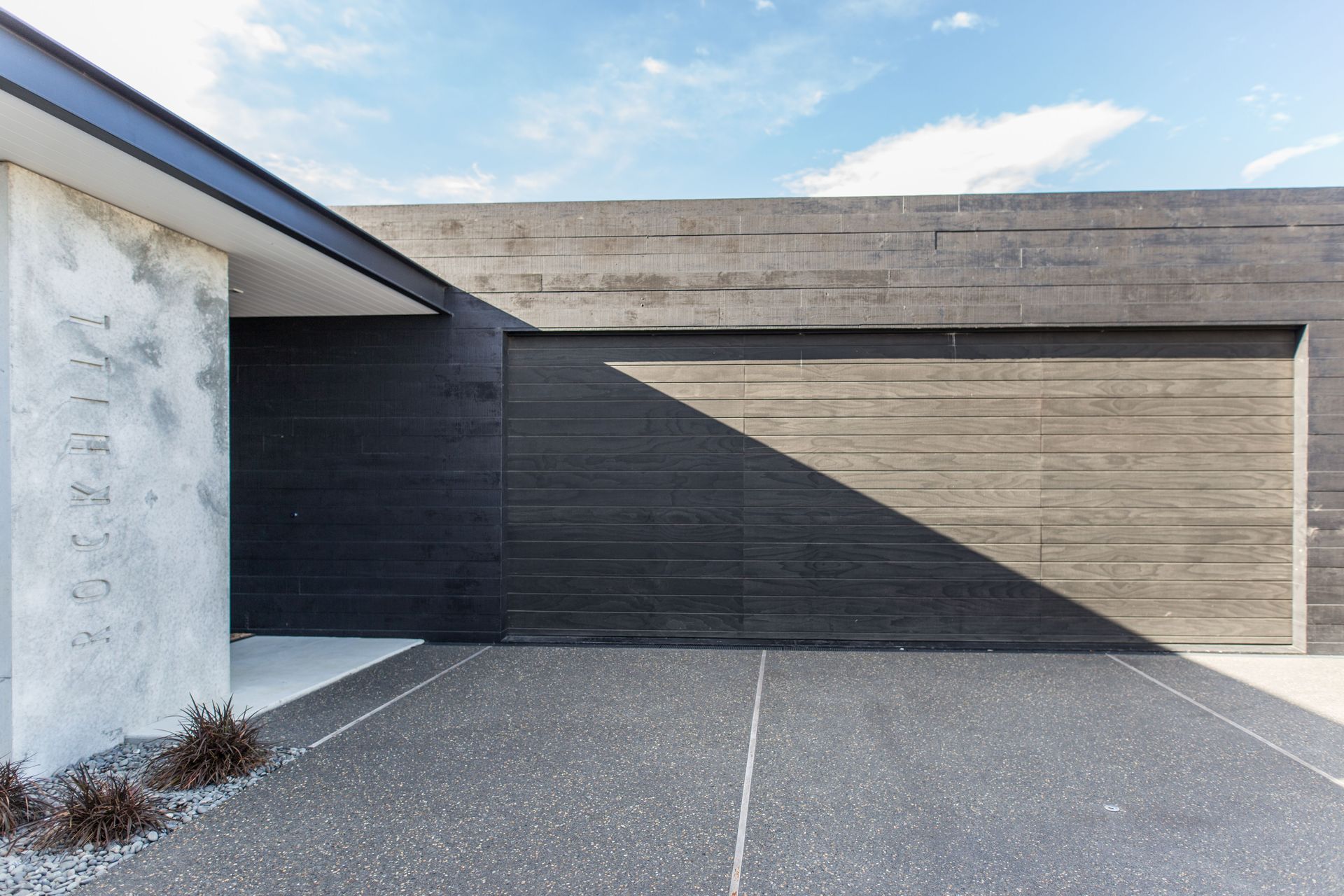 The plan features two separate forms, one private (containing the garage and guest bedrooms) painted black and one public, which has been left as raw concrete.