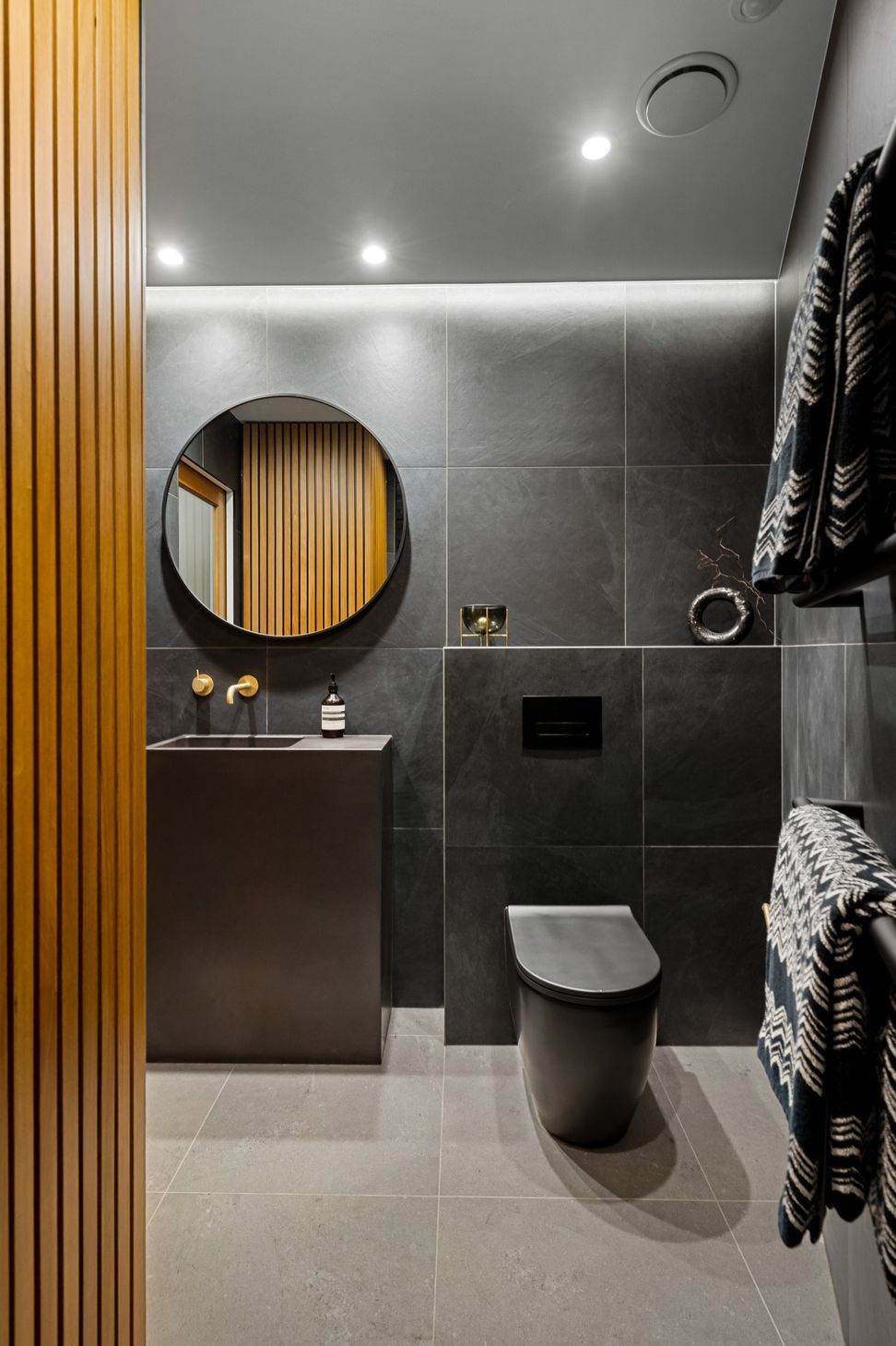 The cupboard features elegant Rimu wood slatted paneling that seamlessly conceals a practical laundry space and additional storage area, combining functionality with aesthetic appeal.
