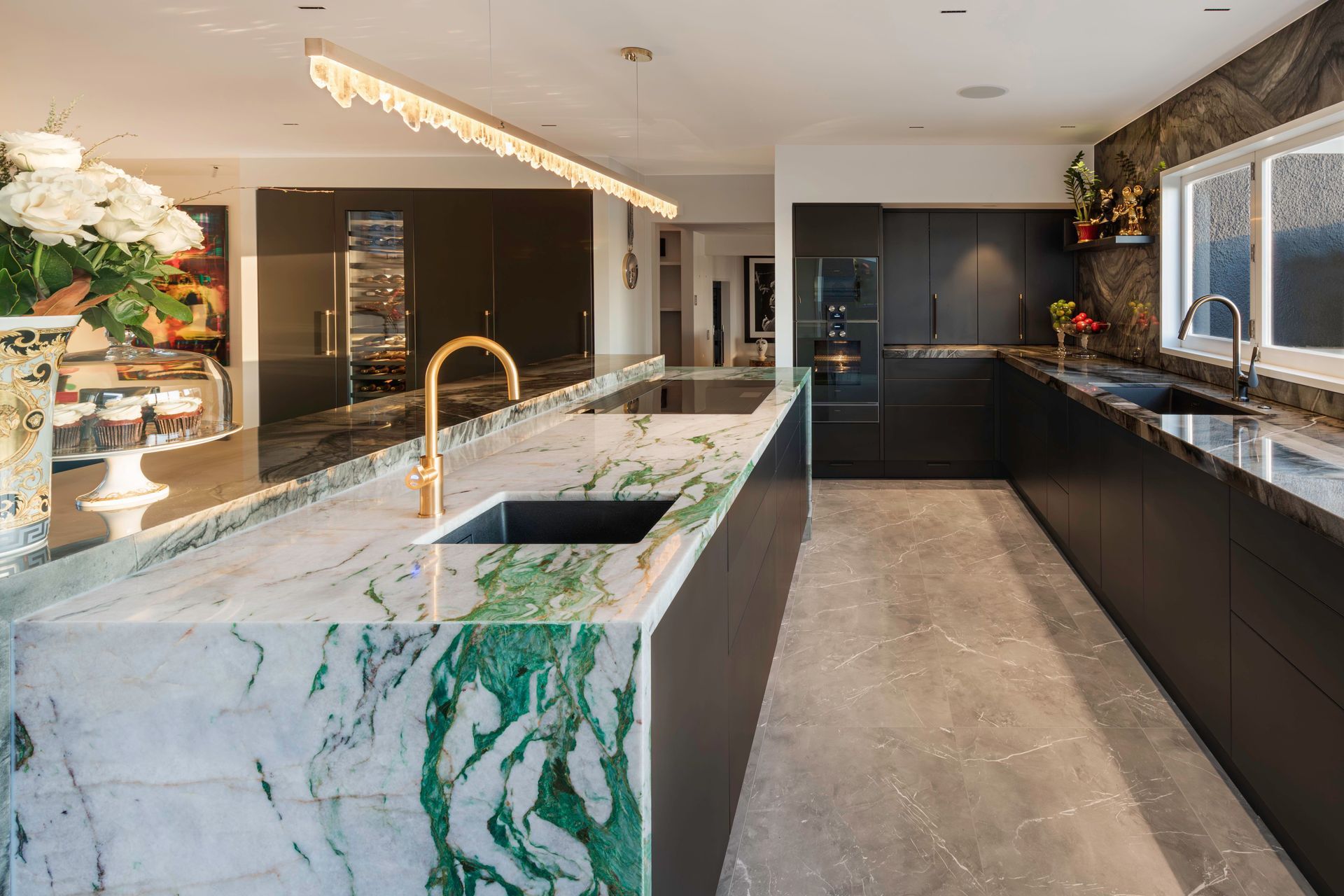 The same stormy charcoal stone is used on the sink bench and walls for a moody textural backdrop to everchanging harbour views. A metal-infused black lacquer is specified for the kitchen’s joinery while anthracite and brass tapware and soft oyster floor tiles complete the rich palette.  The double sinks, fridge, three ovens including a sous vide, and pantry storage are perfectly arranged within the hob-centred zone to allow the home chef efficient flow and access.