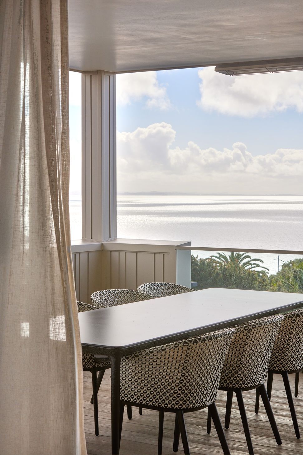 Large sliding doors connect the third-floor living spaces to a generous covered deck designed for outdoor dining and entertaining. The elevated terrace provides a sheltered place to enjoy expansive views across the Hauraki Gulf.
