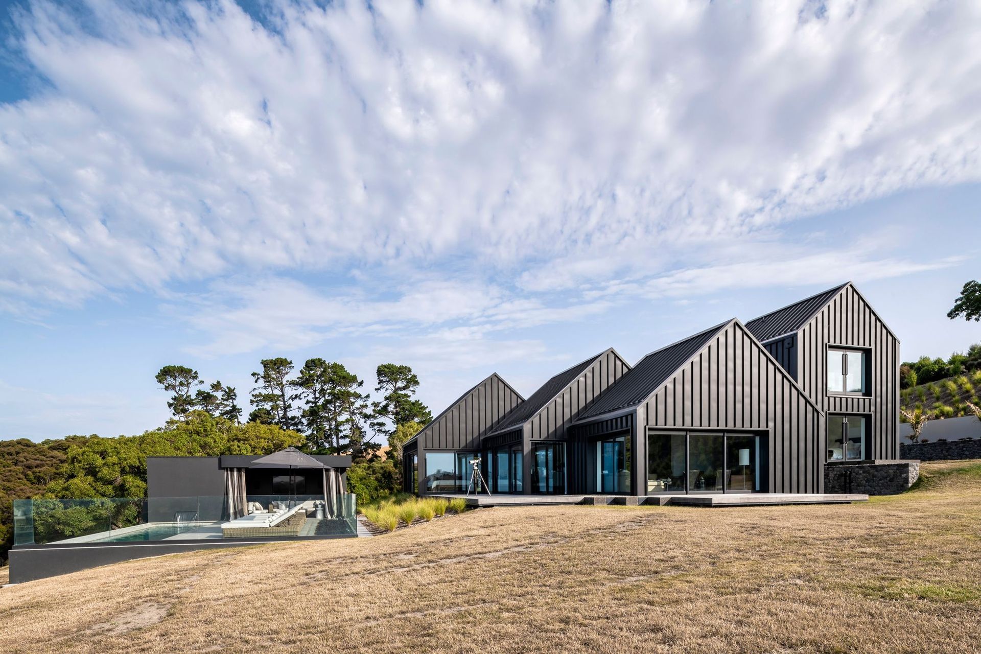 The home with its five striking gable forms, unfurls in the landscape down to a pool and cabana at the bottom of the slope.